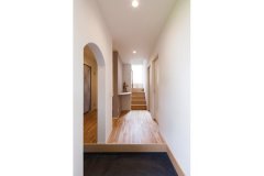 白い壁やバーチの無垢材の柔らかさと、玄関土間のモルタルの落ち着きが融合した玄関部分。家族用の玄関土間のアーチや、飾り棚の曲線が空間に優しい印象をプラスする