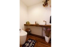 濃い色の床材とドライフラワーがアンティーク感を漂わせるトイレ。幅広の手洗いカウンターも造作