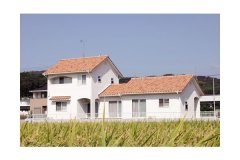 のどかな田園風景の中に建つ、白い塗り壁と赤い屋根がナチュラルな雰囲気の家