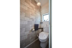 1階のトイレには、奥さまが選んだというコンクリート打ちっぱなし風クロスを貼り、デザイン性の高い空間に仕上げた。