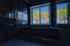 ご主人の要望から、周囲の山景色が楽しめる大きな窓を配したオールブラックの浴室。1日の疲れもほっこり癒やされそう。