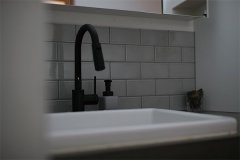 洗面室上部の明かり取りの窓から、柔らかな光が差し込みます。グレーのタイルに実験用シンク、ブラックの蛇口でシックなトーン。