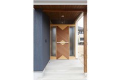 玄関アプローチは庇を大きくとってあるので雨の日も安心。組み木のような斬新なデザインの玄関扉が目を惹く