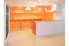 迷いに迷って決めたキッチン背面の壁はオレンジ! ホワイトのレンジフードとNさんが見つけたかわいいペンダント照明との相性はバッチリ。背面にはリ・ライフプロデュースオリジナルの造作棚。4m一枚物の棚板は重厚感があってGOOD!